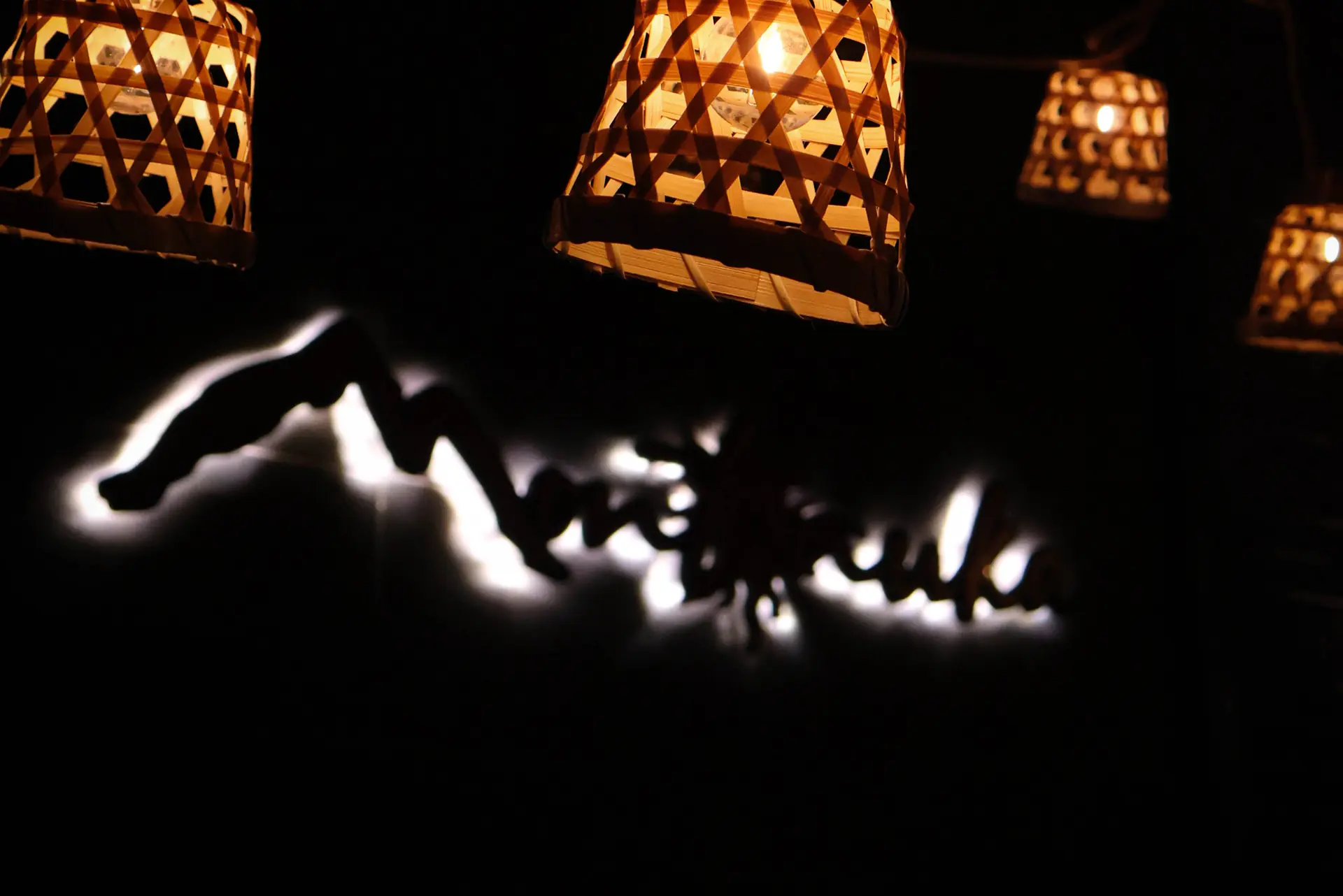 Letrero luminoso con el nombre de Montañuka y silueta de montañas retroiluminada, junto a lámparas colgantes de mimbre encendidas